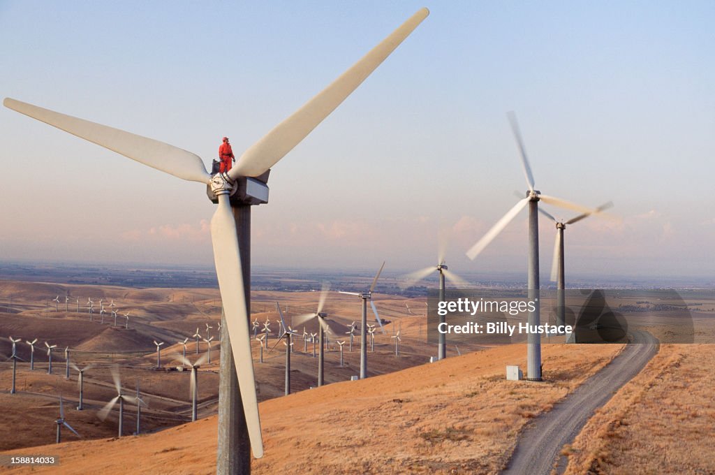 Worker standing on wind turbine at wind farm