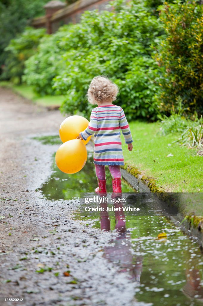 Young girl holding balloons walking in puddles