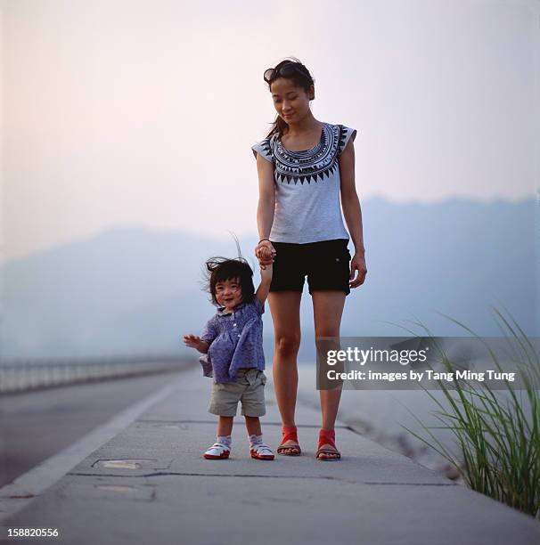 pretty young mother & baby walk along breakwater - mother and daughter in the wind stock-fotos und bilder