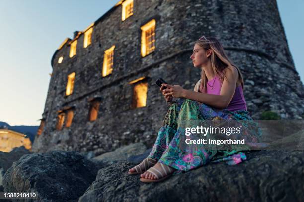 teenager girl sitting on boulders of rapallo harbor and using smartphone - alleen één tienermeisje stockfoto's en -beelden