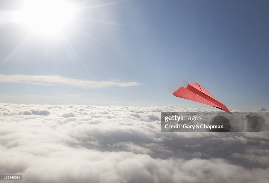 Red paper plane flying high above clouds