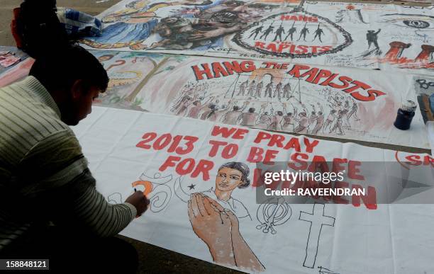 Indian bystanders write on a banner featuring images of 'government and rapists' as it lies on a road in New Delhi on January 1, 2013. The family of...