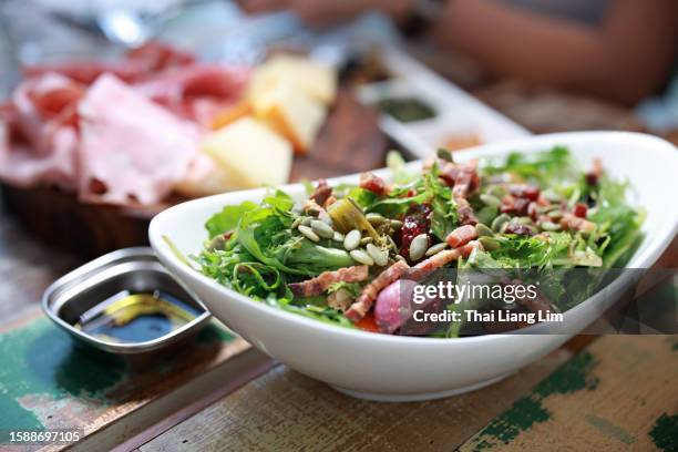 a close-up view of a bowl of fresh salad served alongside antipasto, which is a starter dish in italian cuisine, on a restaurant table. - salad bowl stock pictures, royalty-free photos & images