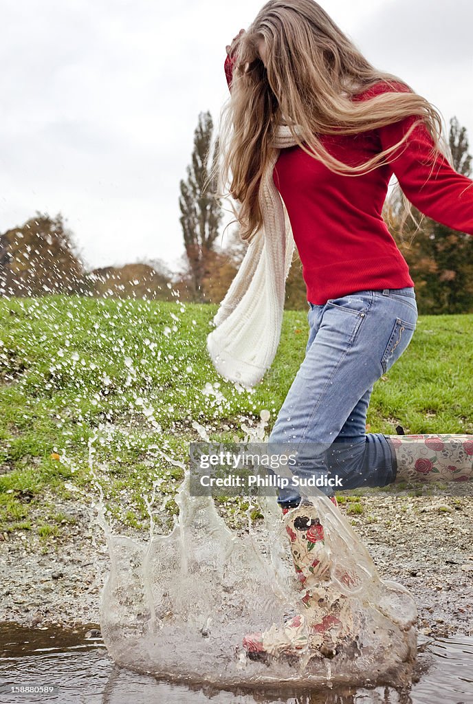 Girl with long blonde hair jumping in puddle