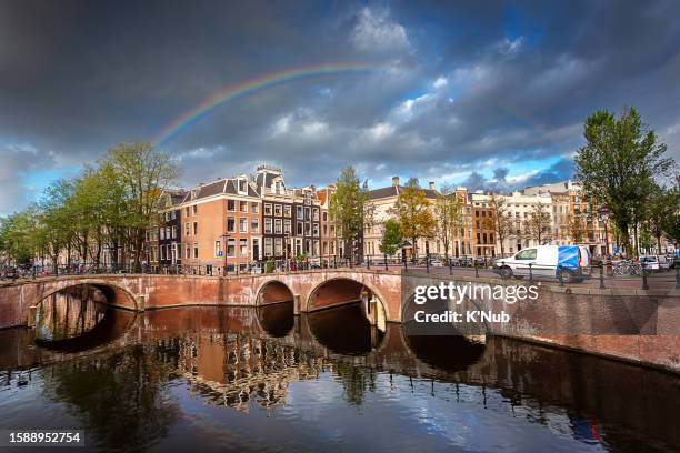 beautiful rainbow on cloudy sky over amsterdam city with old brice over river for boat cruise transportation and road for car and bicycle way where is the famous landmark in amsterdam, netherlands, or holland in europe schengen country - k'nub stock pictures, royalty-free photos & images