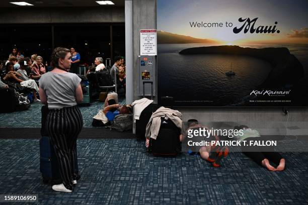 Passengers try to sleep below a "Welcome To Maui" billboard on the floor of the airport terminal while waiting for delayed and canceled flights off...
