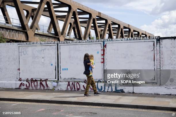Woman carrying a toddler walks past the graffiti wall which was claimed to be painted white by the Tower Hamlets council. On August 5th, the Royal...
