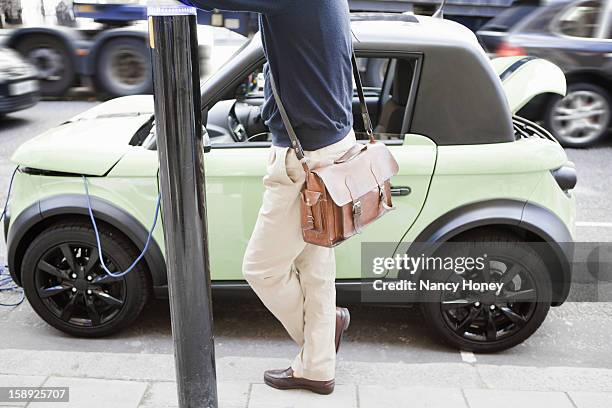 man charging electric car on city street - nancy green stock pictures, royalty-free photos & images