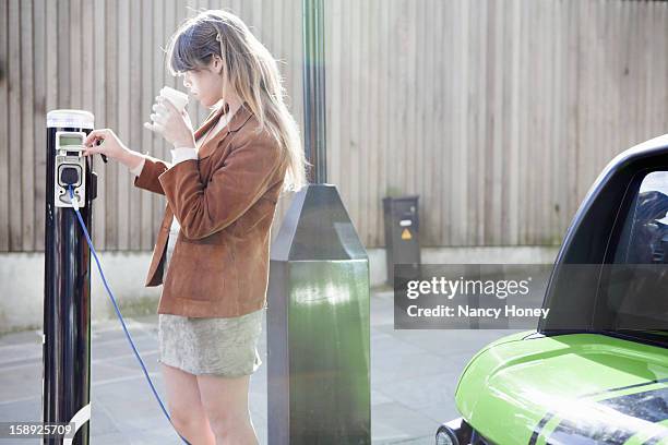 woman charging electric car on street - elektroauto mensch stock-fotos und bilder