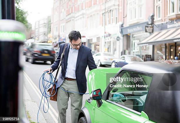 man charging electric car on street - nancy green fotografías e imágenes de stock