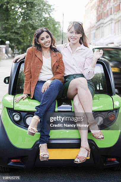 women sitting on car on city street - nancy green stockfoto's en -beelden