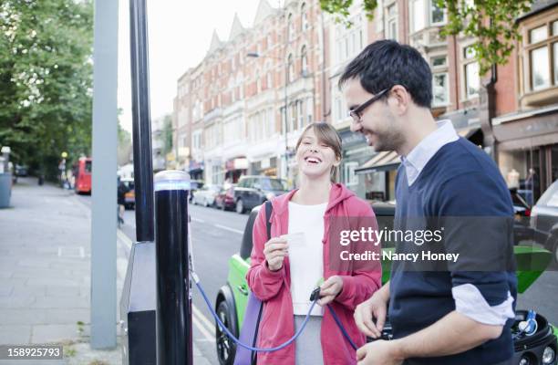 Couple Charging Electric Car On Street, Stockfoto