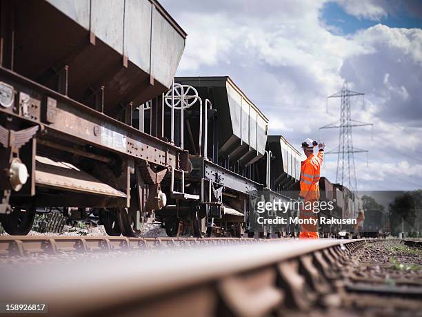 railway worker wearing high visibility clothing waving alongside train - schienenverkehr stock-fotos und bilder
