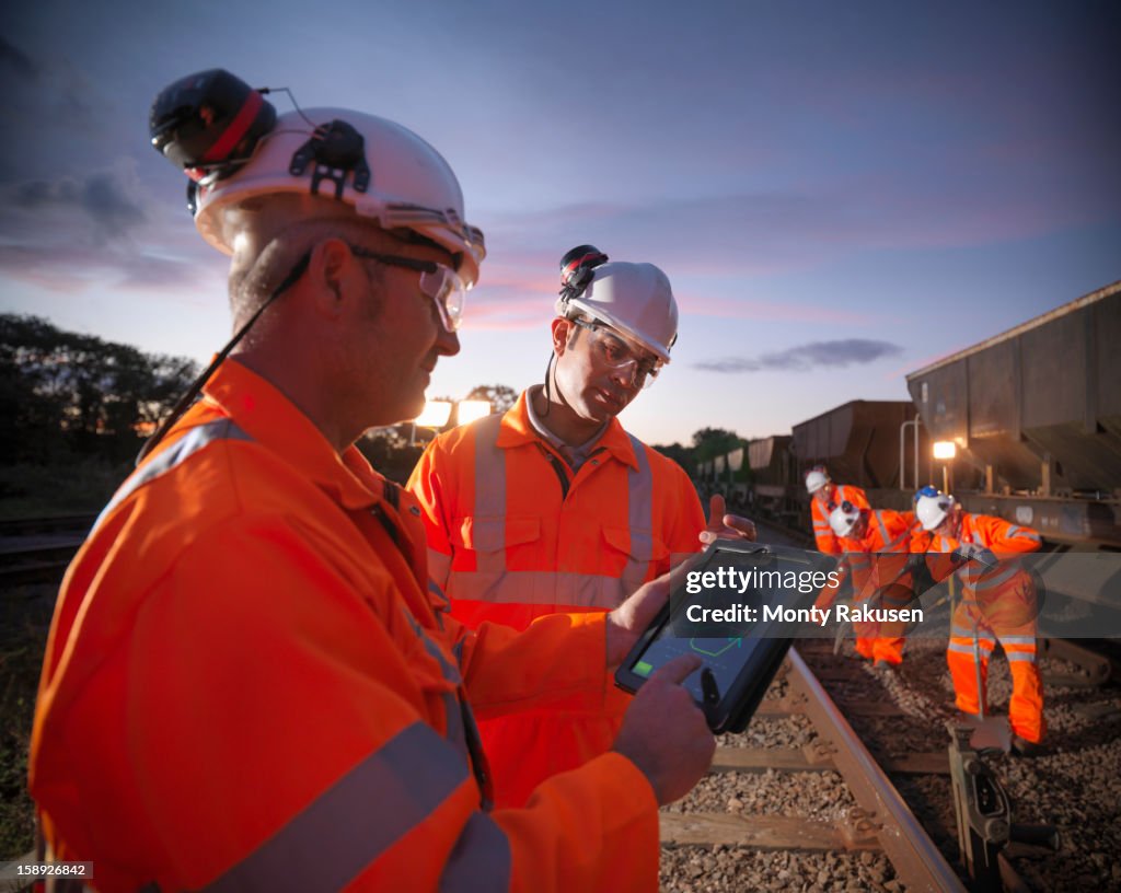 Railway workers using digital tablet to view work details on railway tracks