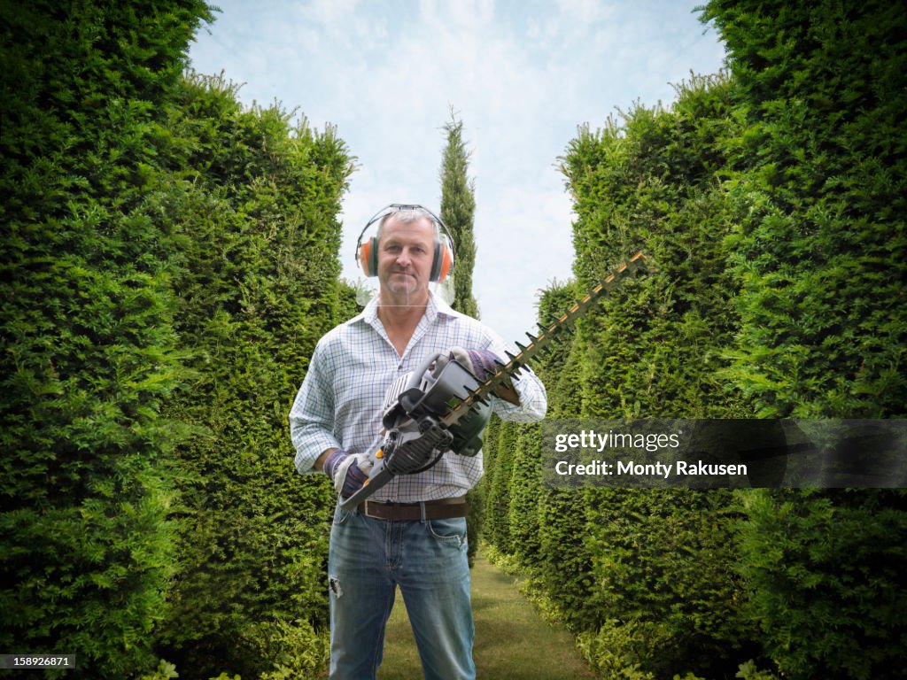 Portrait of gardener wearing ear protectors and visor holding hedge trimmer