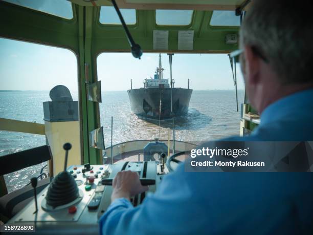 view over the shoulder of captain at the  bridge of tugboat towing ship at sea - boat captain stock pictures, royalty-free photos & images