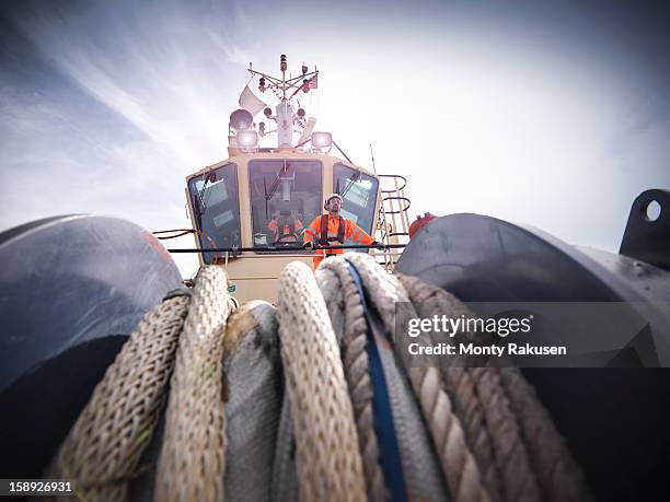 tug workers wearing protective clothing on tug, rope in foreground - tug boat stock pictures, royalty-free photos & images