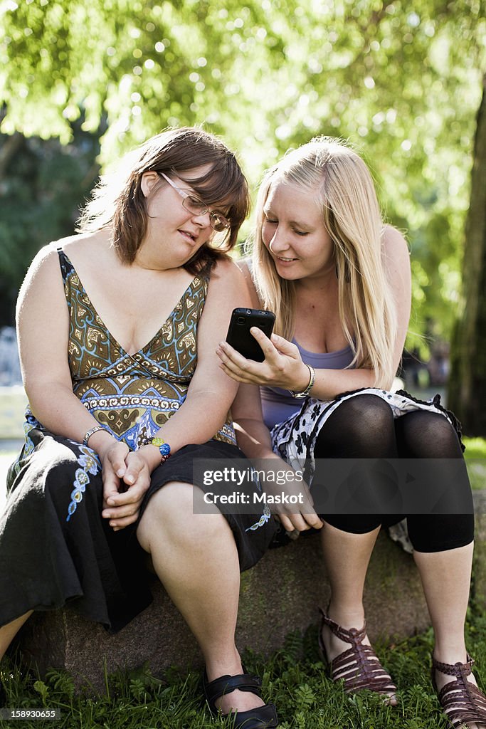 Caring woman with down syndrome showing mobile phone to her personal assistant