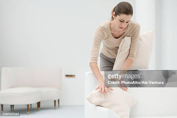 woman arranging pillows on sofa - arrangiare foto e immagini stock