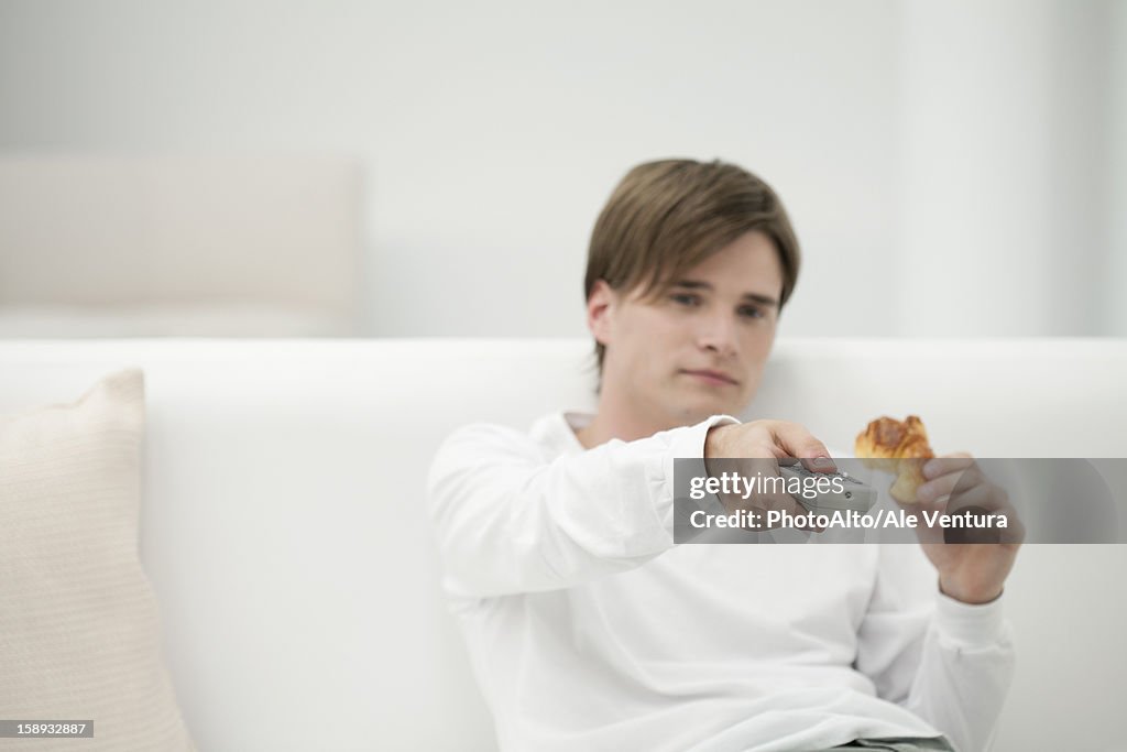 Young man watching TV, changing channel with remote control