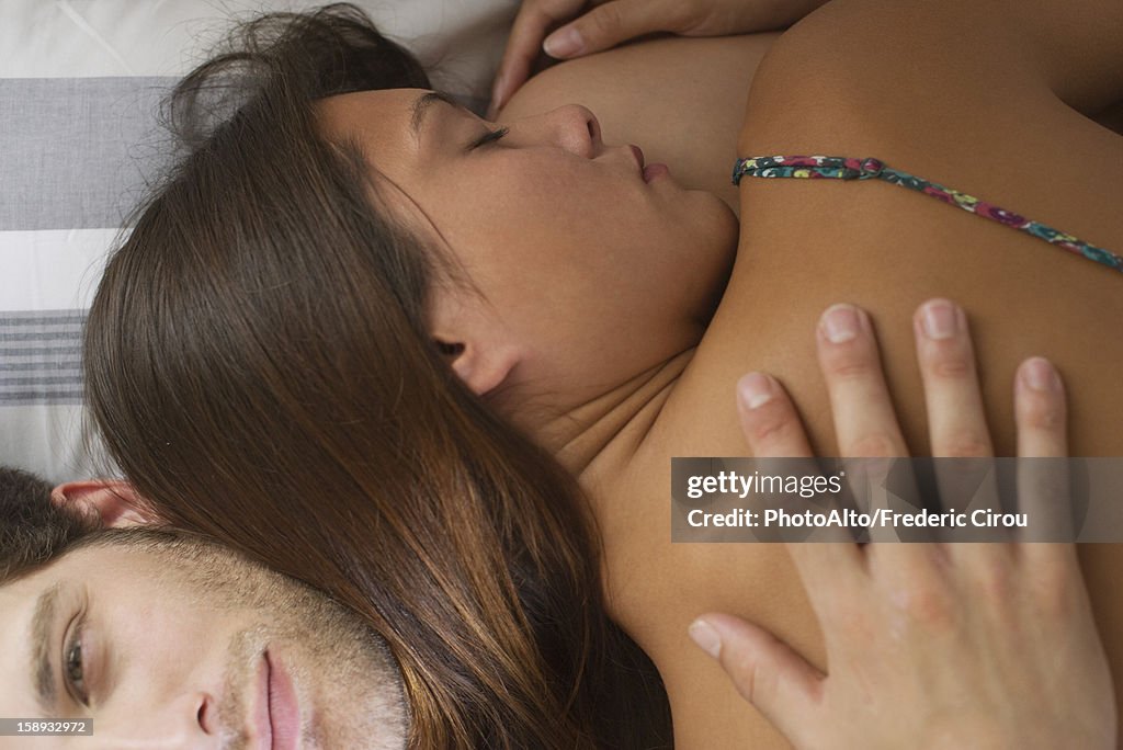 Young woman embracing boyfriend in bed with eyes closed. directly above