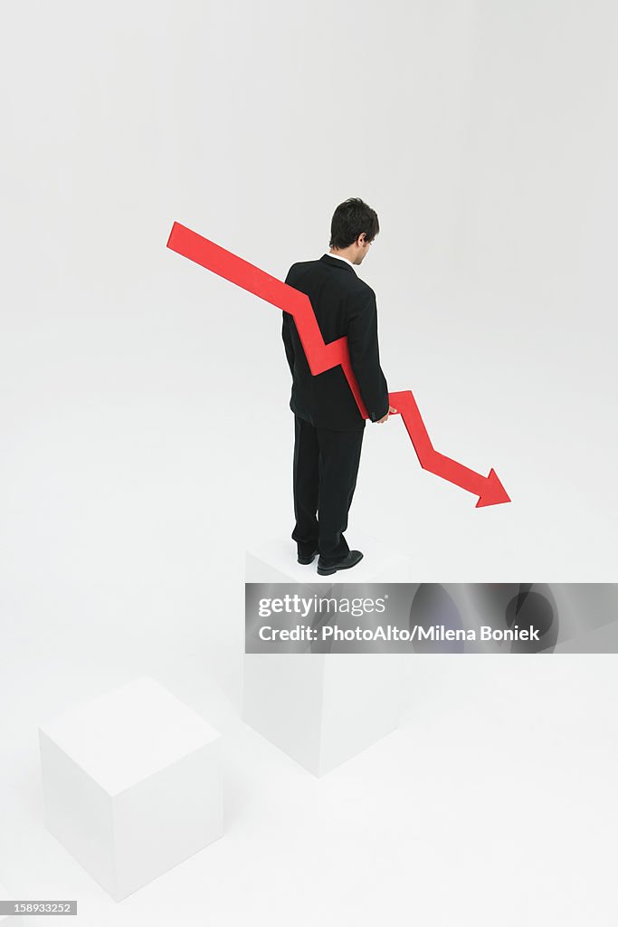 Businessman standing at top of steps holding arrow pointed downward