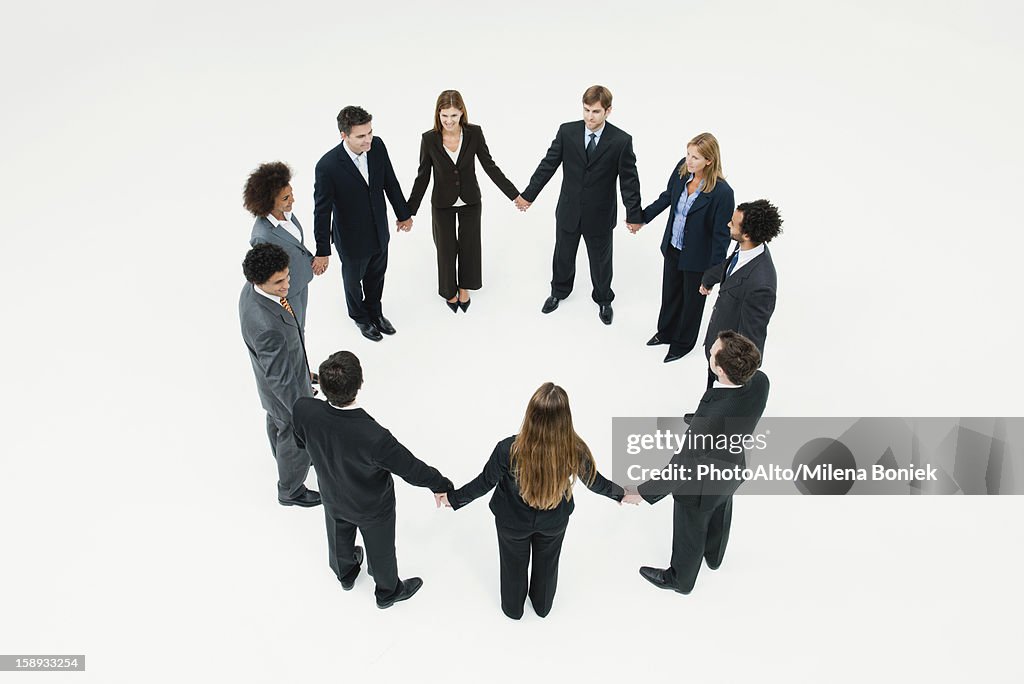 Businessmen and businesswomen standing together in circle holding hands