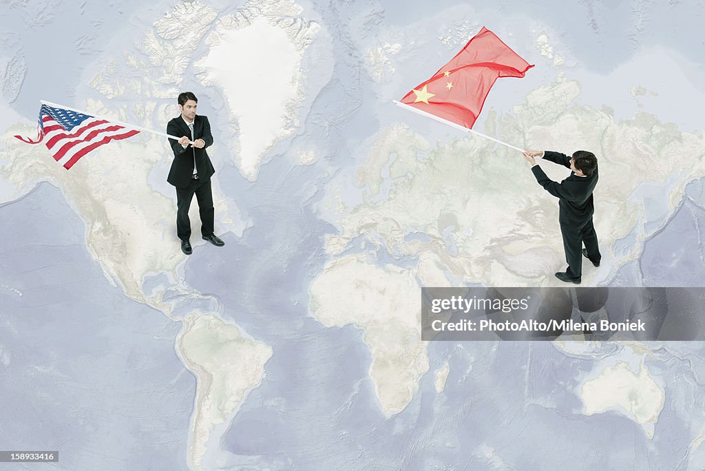 Businessmen standing on world map, waving American and Chinese flags