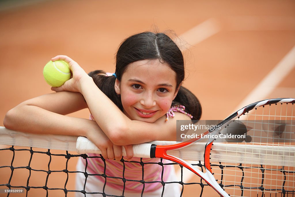 Young Girl Leaning On Net In Tennis Court