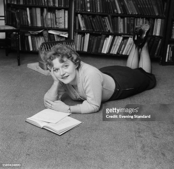 Scottish novelist Muriel Spark reading while lying on the floor, May 25th 1960.