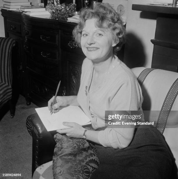 Scottish novelist Muriel Spark making notes while sitting in an armchair, May 25th 1960.