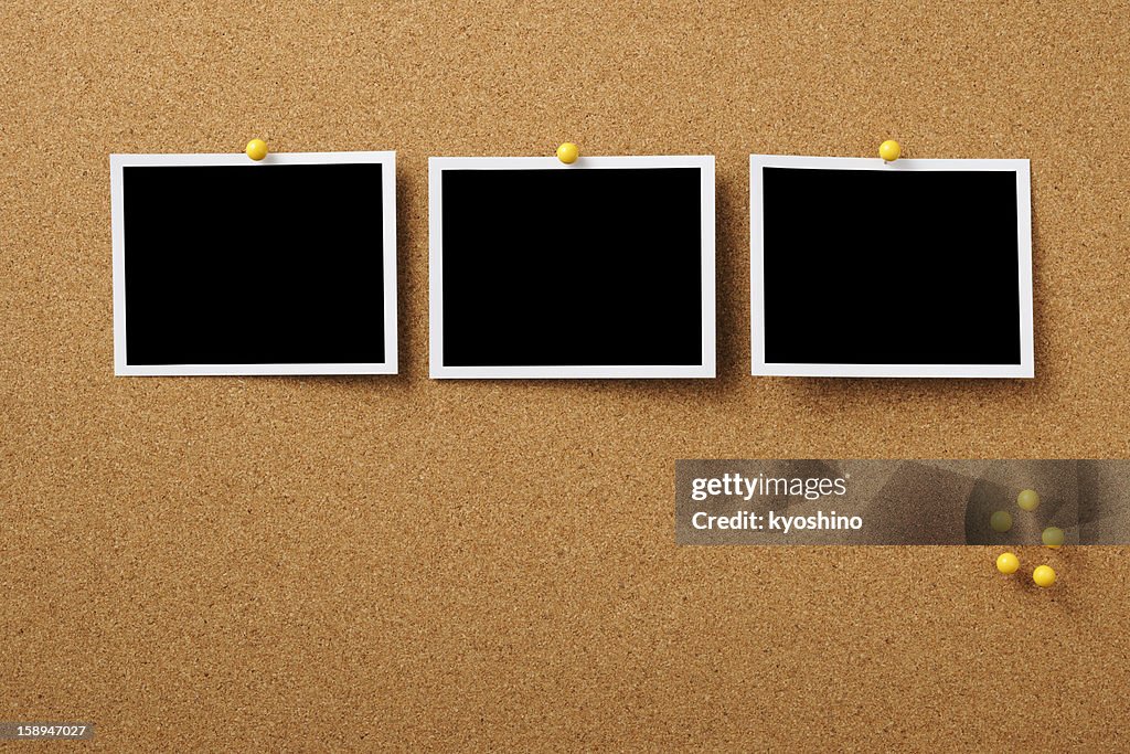 Three blank Polaroid pinned on cork board with yellow thumbtack