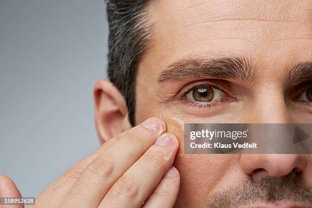 man putting anti wrinkle gel around the eyes - putting lotion stock pictures, royalty-free photos & images