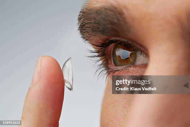 close up of man putting in contact lens - lenti a contatto foto e immagini stock