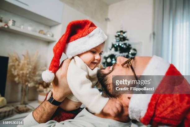 millennial-mann mit kleinem kind mit weihnachtsmannmütze - baby christmas stock-fotos und bilder