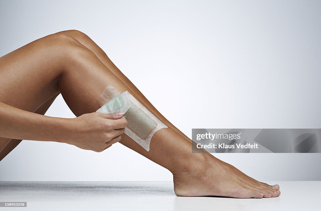 Woman removing hair on the leg with wax strip