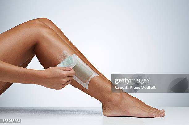 woman removing hair on the leg with wax strip - waxing hair removal stock pictures, royalty-free photos & images