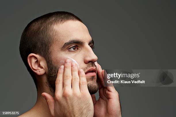 man rubbing skin cream on the cheeks - beauty studio moisturisers stock-fotos und bilder