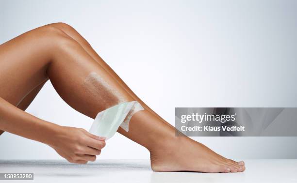 woman removing hair on the leg with wax strip - waxing stock-fotos und bilder