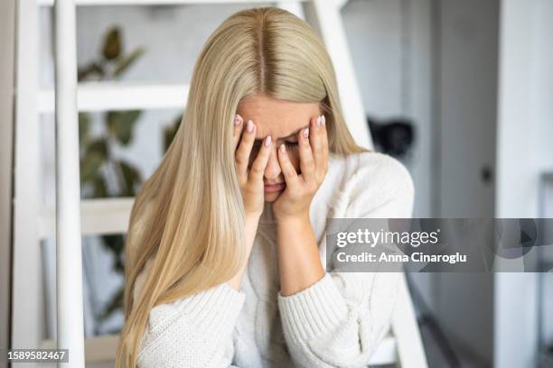sad blonde girl sitting on the stairs at home. depressive mood - bedauern stock-fotos und bilder
