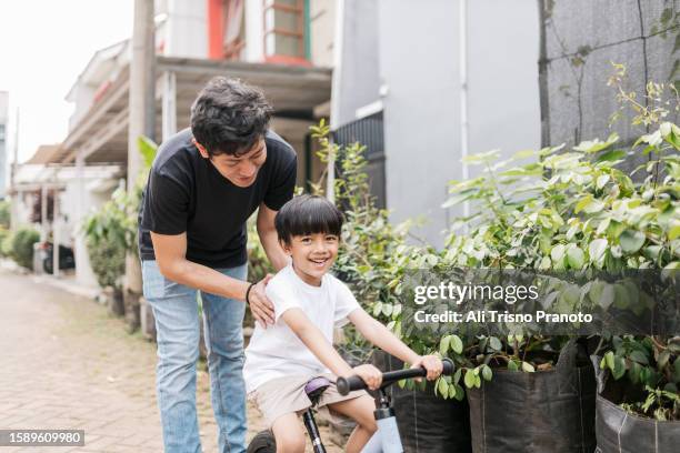 young father accompanying his son riding a bike - banten stock pictures, royalty-free photos & images