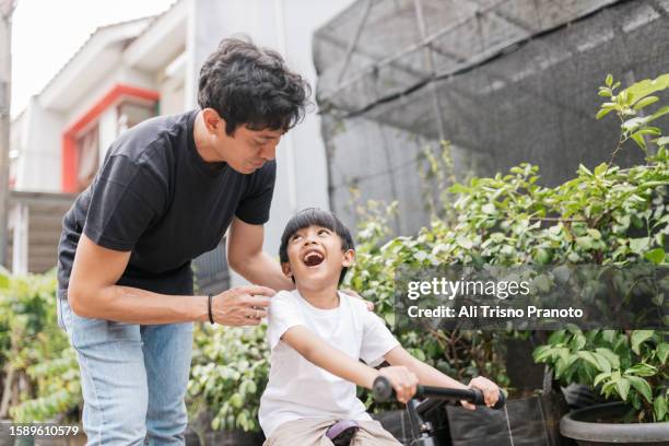 young father accompanying his son riding a bike - indonesischer archipel stock-fotos und bilder