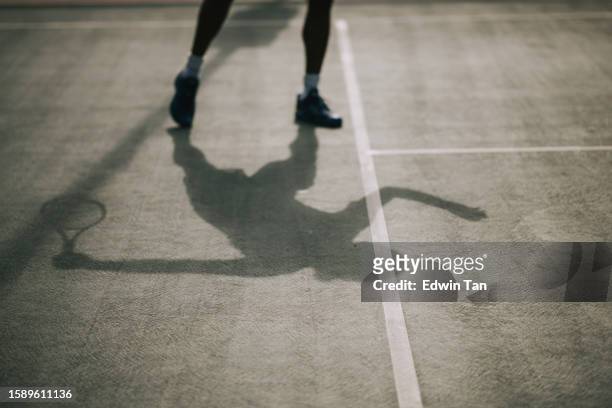 tenista asiático de sombra larga listo para servir la pelota en la cancha de tenis - 50 sombras fotografías e imágenes de stock