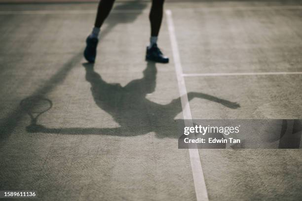 lunga ombra tennista asiatica pronto a servire la palla nel campo da tennis - tennis shadow foto e immagini stock