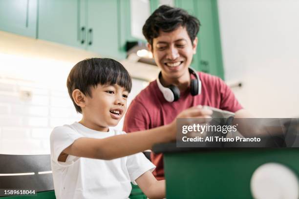 young father  sitting together with his boy in the island table in the kitchen. father watching his boy using mobile phone - banten stock pictures, royalty-free photos & images