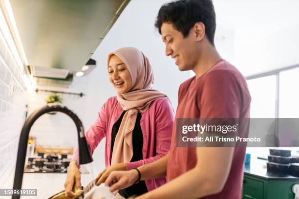 young husband and wife washing the dishes together, at home - asiático de asia sudoriental fotografías e imágenes de stock