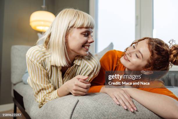 dos jóvenes amigas acostadas en un sofá y mirándose alegremente - fond orange fotografías e imágenes de stock