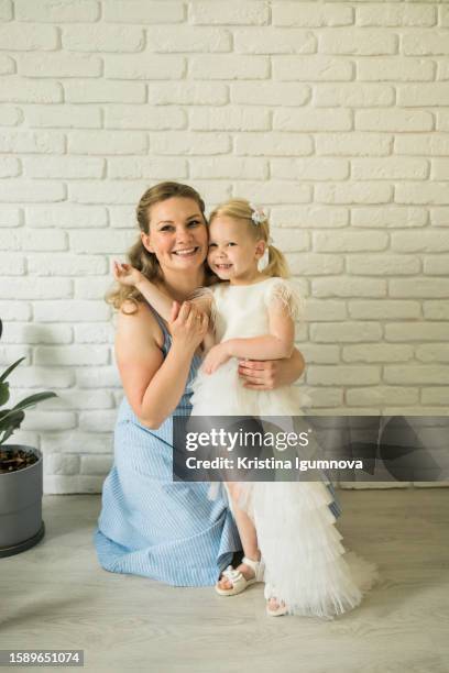 mother and child girl in a festive princess dress smile and hug in the room against  background brick wall. dress on first communion - baptism party stock pictures, royalty-free photos & images