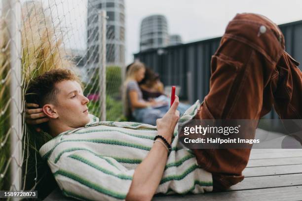 portrait of young stylish generation z boy browsing on smartphone. - überkreuzte beine stock-fotos und bilder