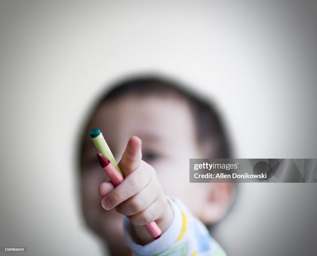 Toddler holding crayons and pointing index finger